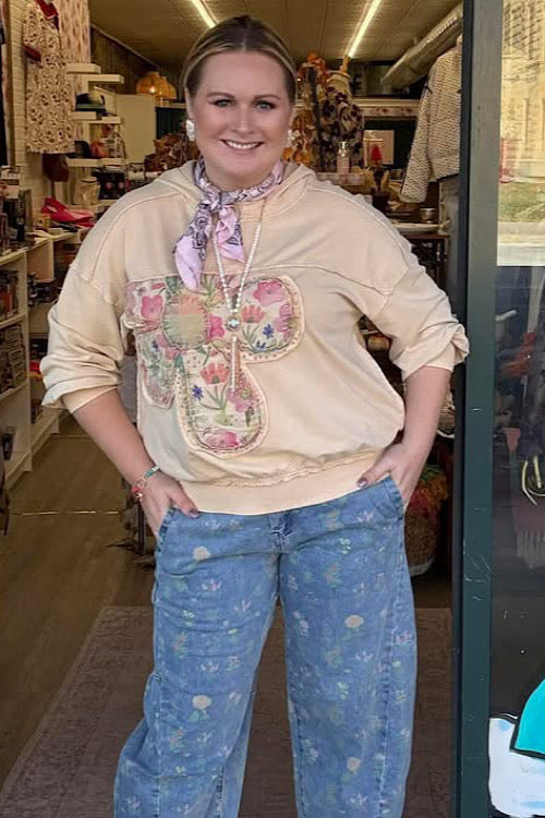Woman wearing a beige blouse with floral embroidery and blue patterned pants in a store setting.