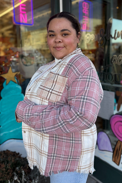 Person wearing a plaid shirt and scarf standing in front of a store window with neon signs.