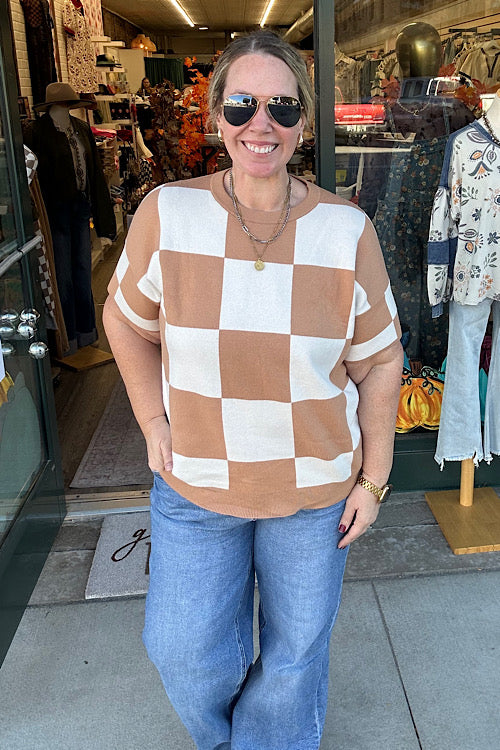Woman wearing a checkered shirt and sunglasses standing in front of a store entrance.