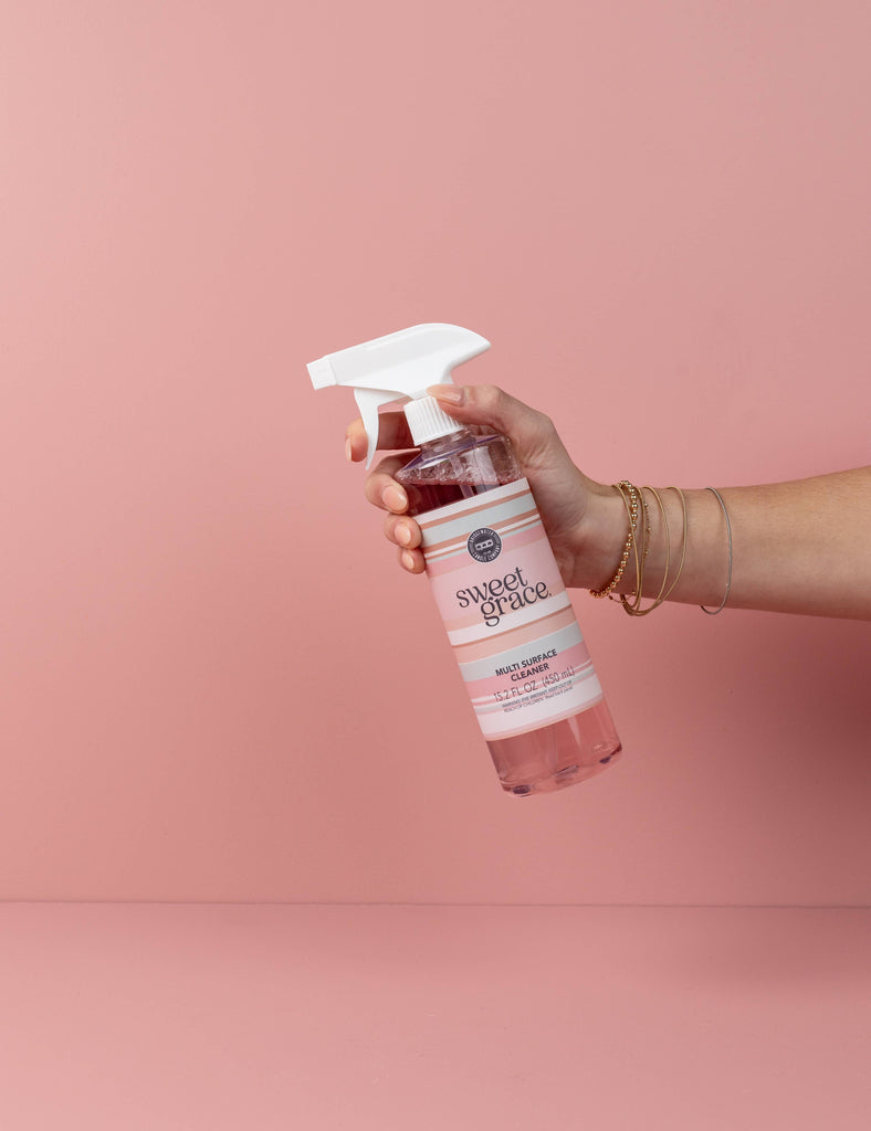 Hand holding a 'sweet peace' spray bottle against a pink background