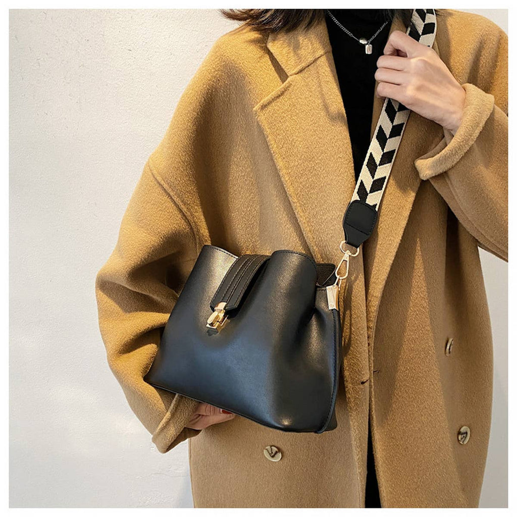Person wearing a tan coat holding a black handbag with a patterned strap.