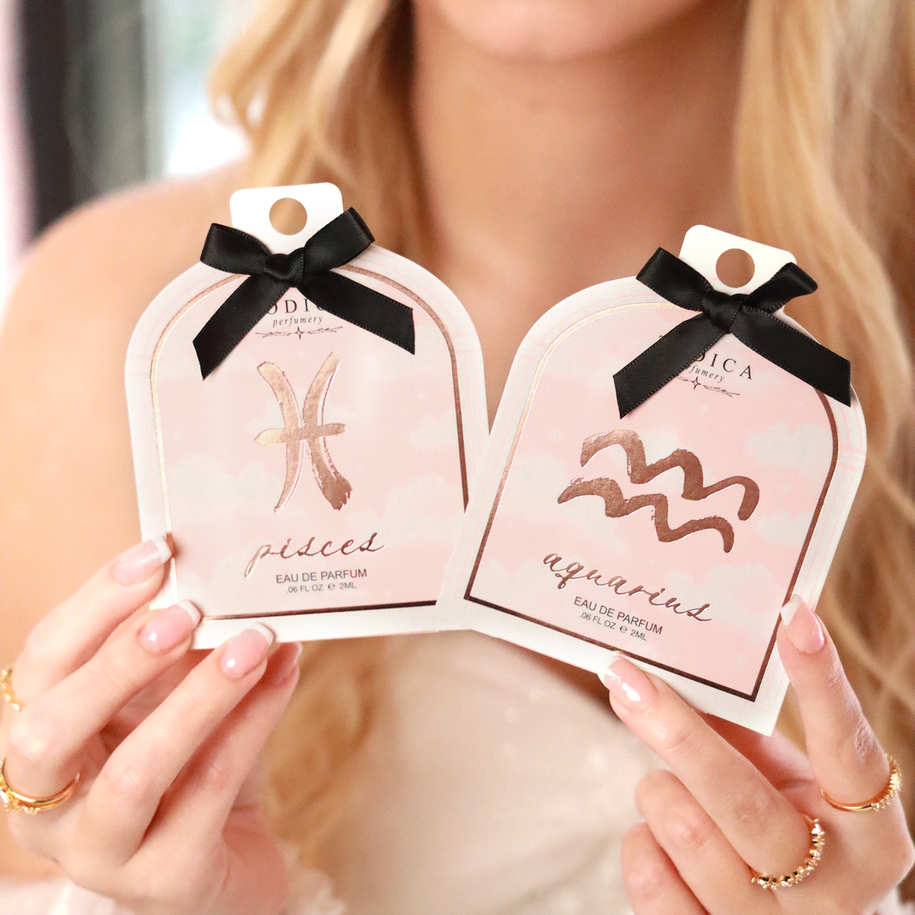Two zodiac-themed perfume packages held by a person with a blurred background