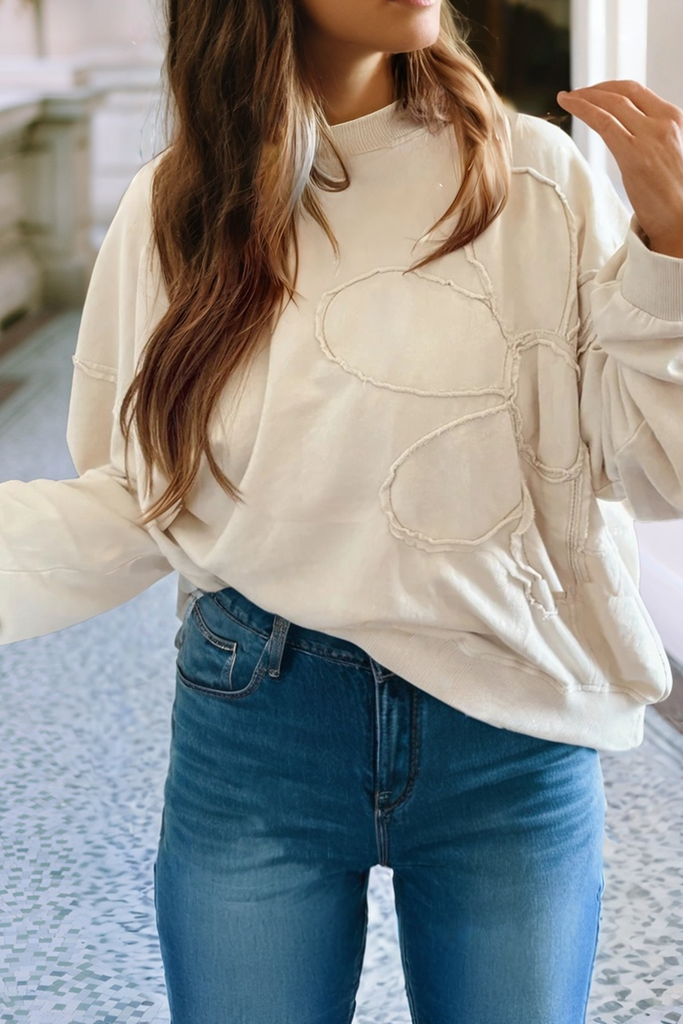 Person wearing a beige sweatshirt with a heart design and blue jeans indoors.