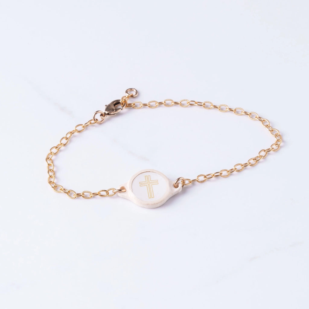 Gold bracelet with a circular charm featuring a cross on a light gray background