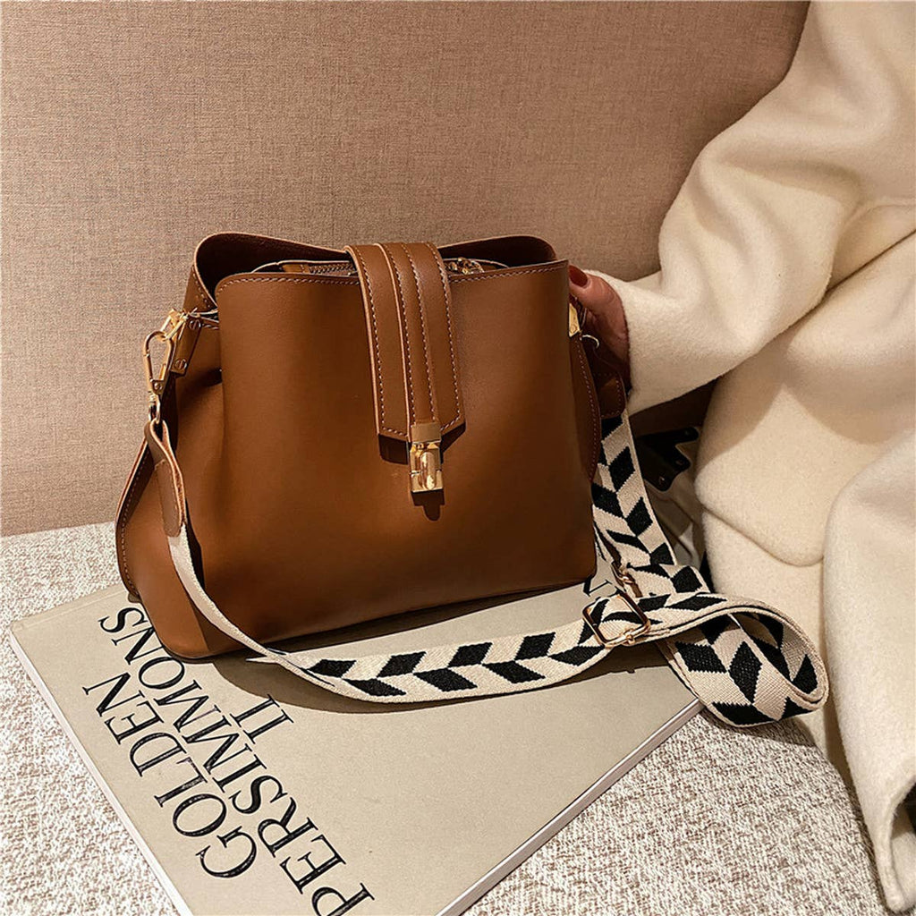 Brown handbag with a patterned strap on a surface with a beige background