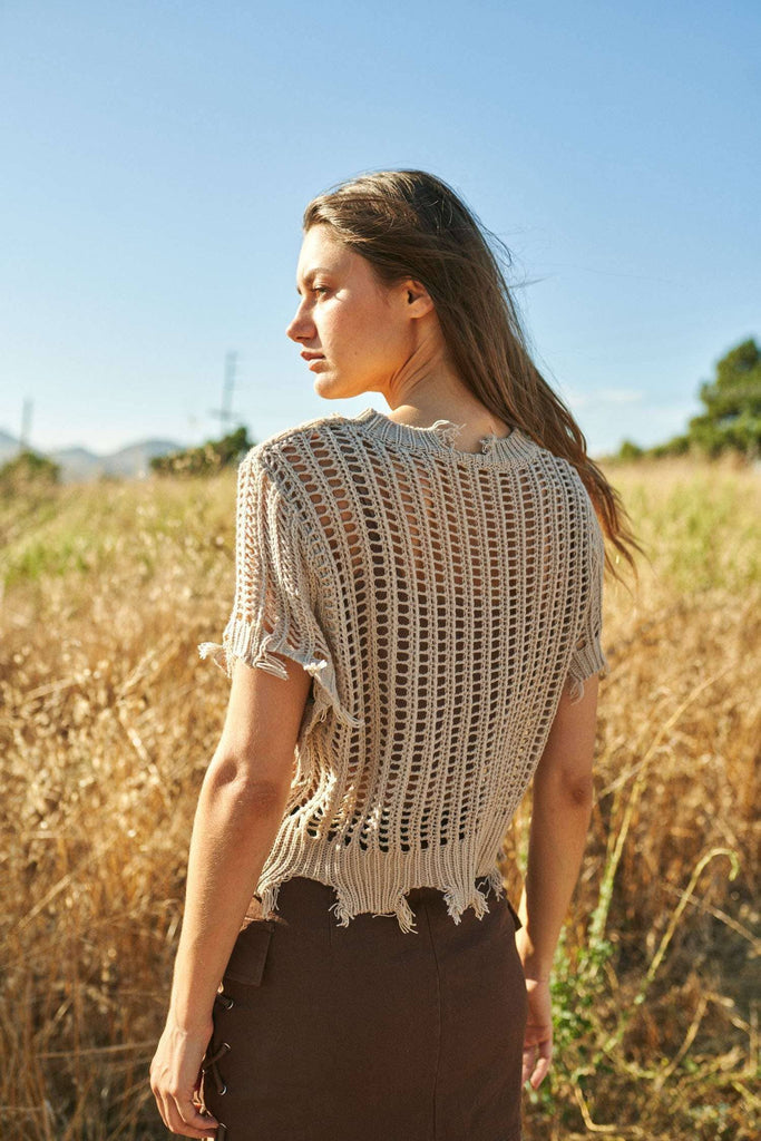 Woman wearing a crochet top in a field with a clear blue sky.