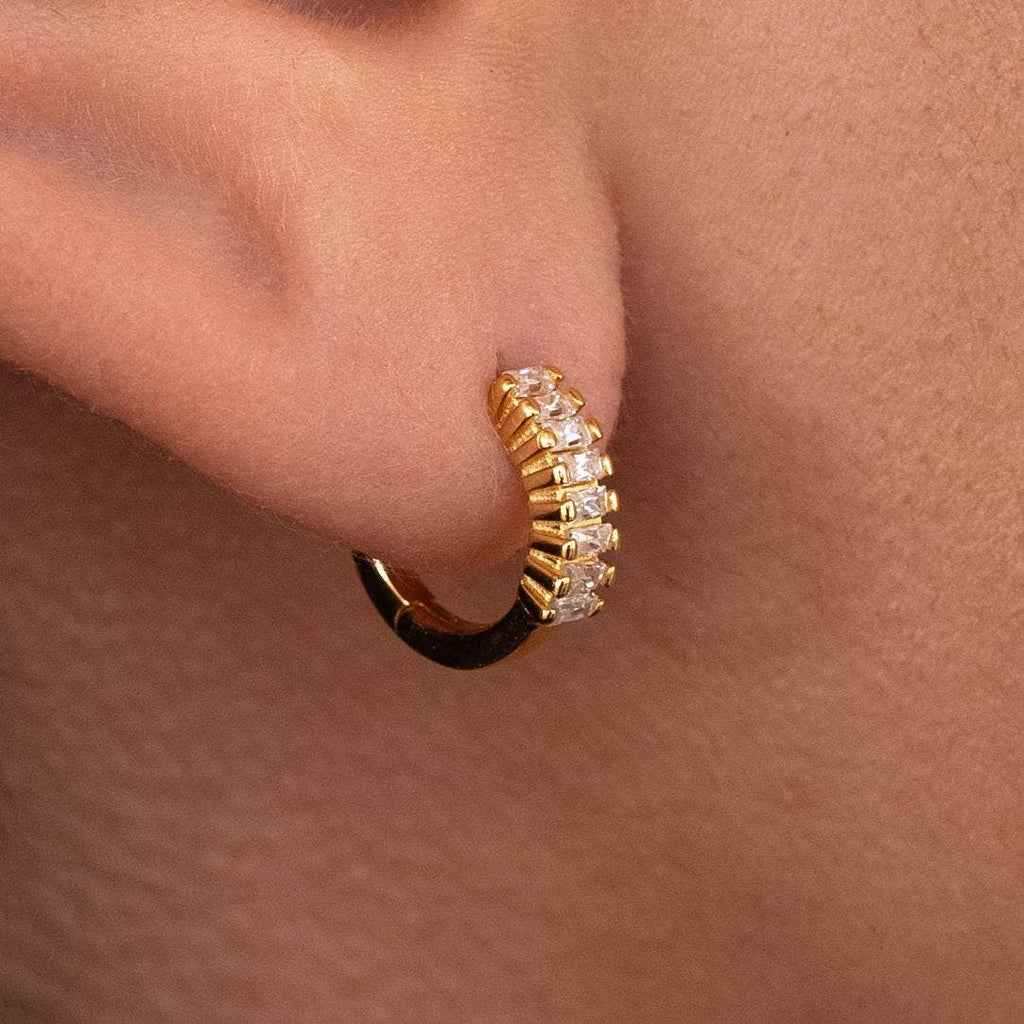 Gold hoop earring with small diamonds worn by a person.