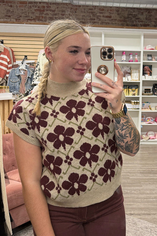 Person wearing a patterned sweater taking a mirror selfie in a store.