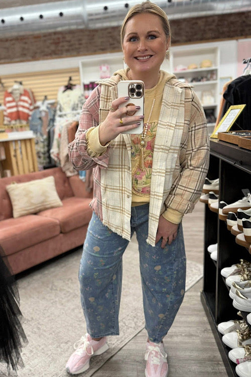 Person taking a selfie in a store wearing a plaid jacket, yellow top, and blue jeans.