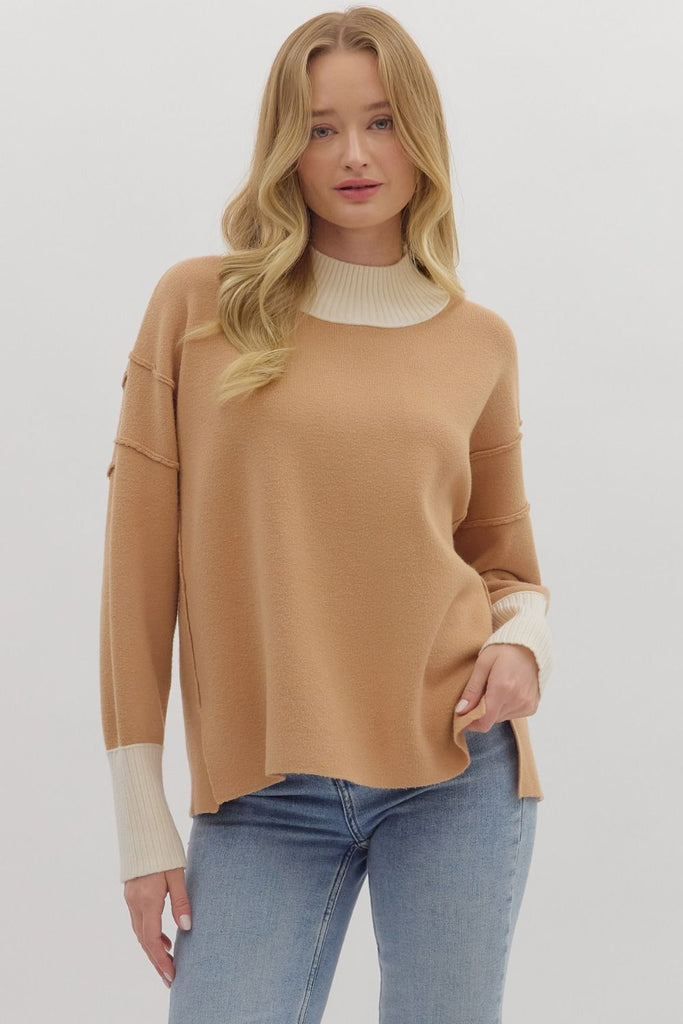 A woman wears a two-toned knit sweater with a camel-colored body and a contrasting cream ribbed turtleneck and cuffs. She is wearing it with blue jeans.