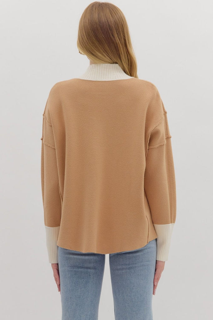 A woman wears a two-toned knit sweater with a camel-colored body and a contrasting cream ribbed turtleneck and cuffs. She is wearing it with blue jeans.