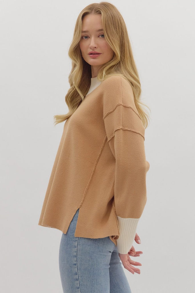 A woman wears a two-toned knit sweater with a camel-colored body and a contrasting cream ribbed turtleneck and cuffs. She is wearing it with blue jeans.