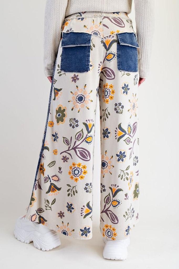 Annelise floral patchwork wide-leg pants on an ecru background with denim pocket accents, styled with a drawstring waist and chunky white sneakers.