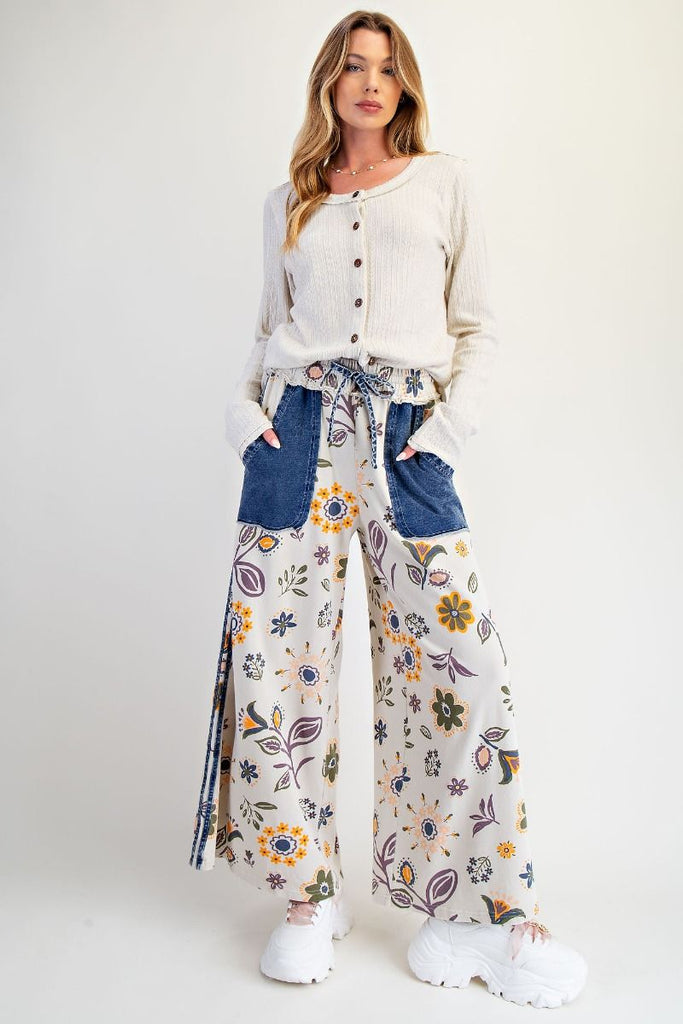 Annelise floral patchwork wide-leg pants on an ecru background with denim pocket accents, styled with a drawstring waist and chunky white sneakers.
