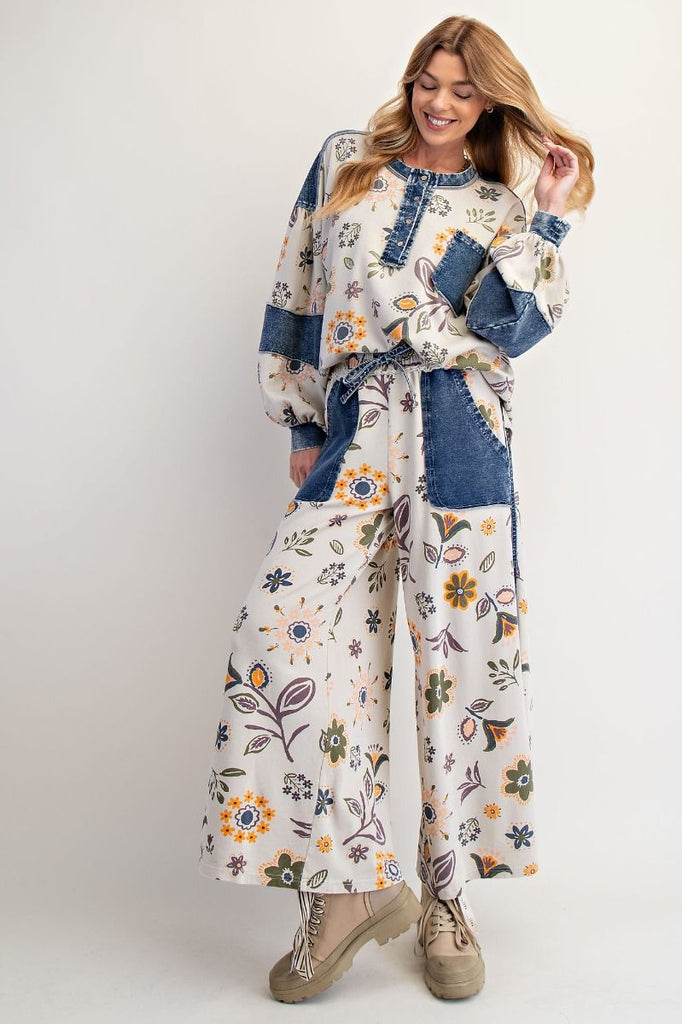 Annelise floral patchwork wide-leg pants on an ecru background with denim pocket accents, styled with a drawstring waist and chunky white sneakers.