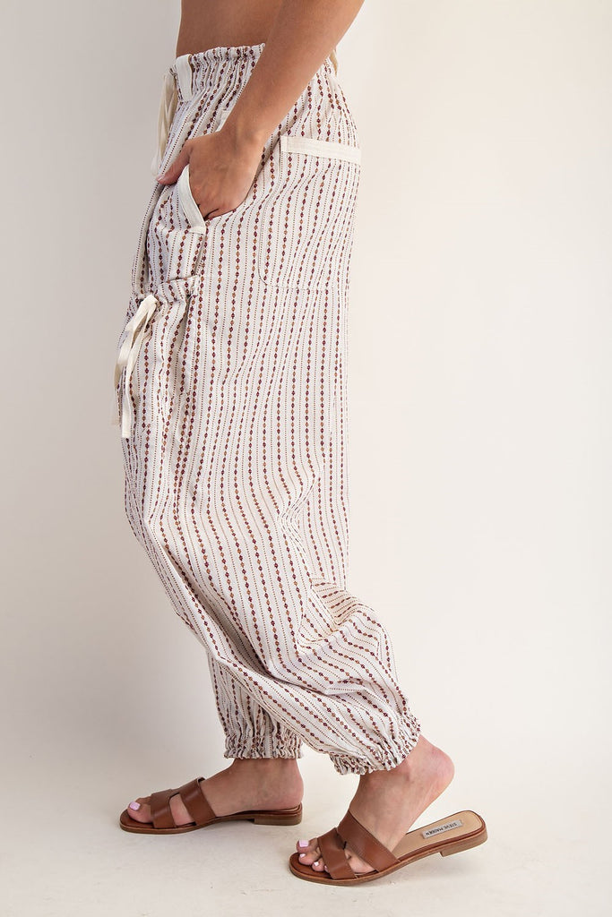 Oatmeal jogger pants with a micro diamond stripe pattern, elastic waistband with contrast drawstring, oversized belt loops, side and back pockets, cargo pockets with cinch ties, and elasticized cuffs