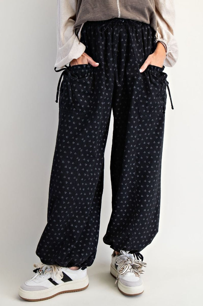 Black mineral-washed wide-leg pants with tonal floral print, elastic drawstring waist, front patch pockets, and adjustable drawstring hems