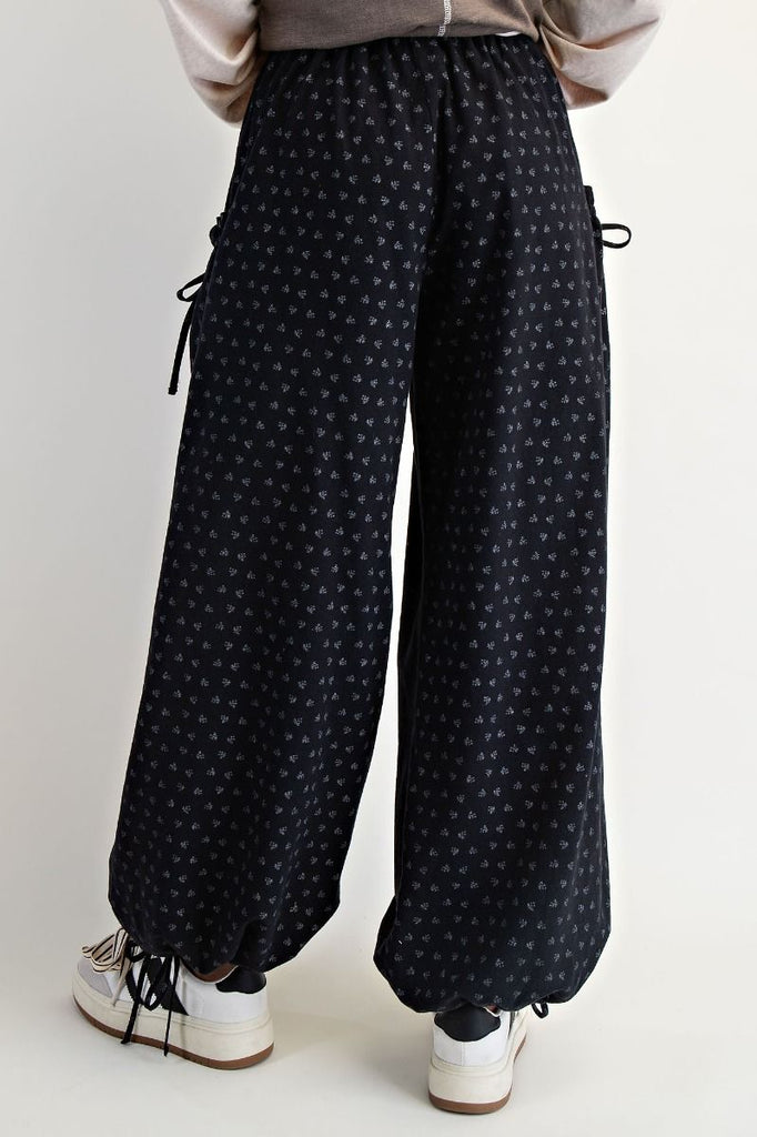 Black mineral-washed wide-leg pants with tonal floral print, elastic drawstring waist, front patch pockets, and adjustable drawstring hems