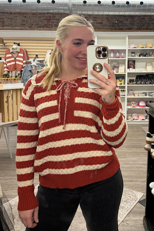 Person wearing a red and white striped sweater taking a mirror selfie in a store.