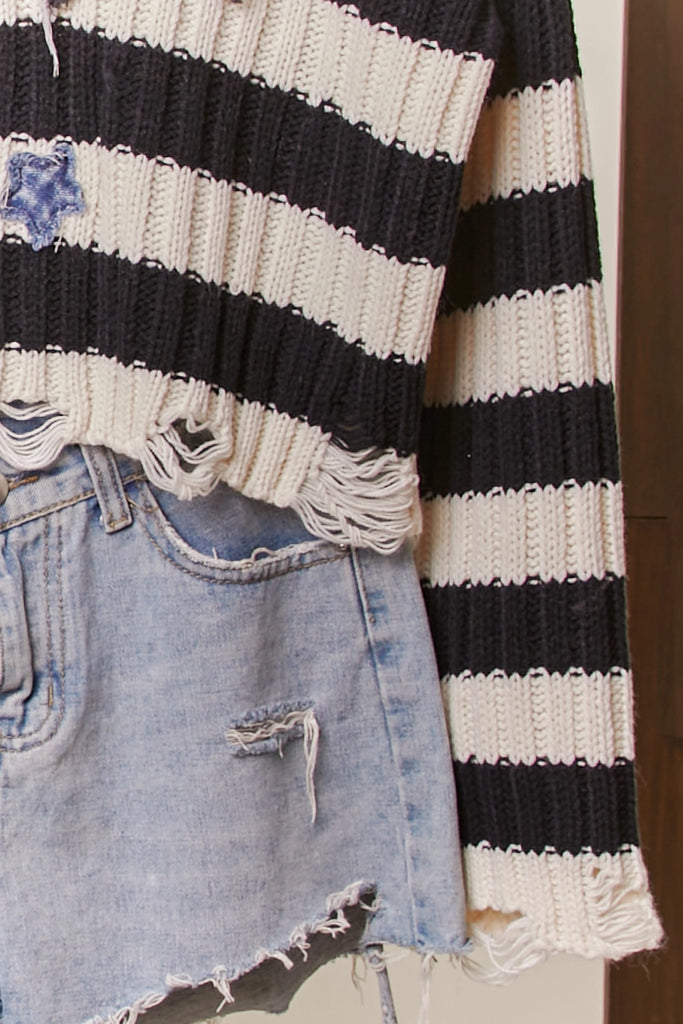 Black and cream striped distressed sweater with star patch and frayed hemline, cropped fit.