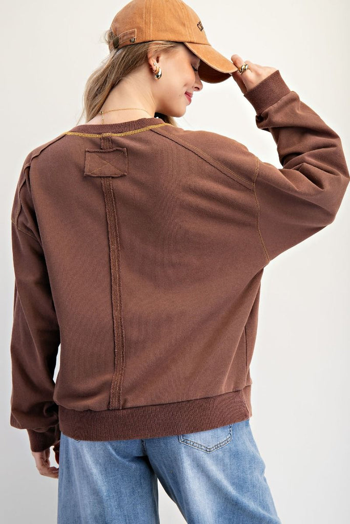 A mocha-colored washed terry pullover with a relaxed fit, featuring patchwork "USA" lettering on the front, dropped shoulders, ribbed cuffs and hem, and contrast topstitching at the neckline.