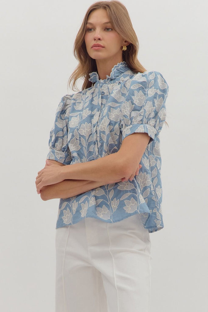 A chambray-colored short puff-sleeve top with white botanical embroidery, a ruffled stand-up collar, and a button-down front.