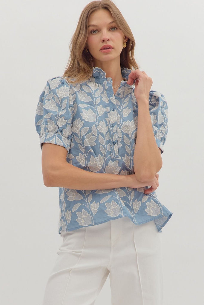 A chambray-colored short puff-sleeve top with white botanical embroidery, a ruffled stand-up collar, and a button-down front.