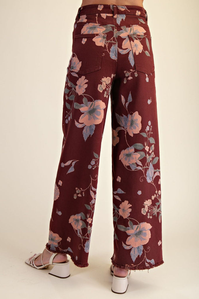 Model wearing Easel Calluna floral twill pants in burgundy with soft pink and blue botanical print, featuring high waist and straight leg silhouette.