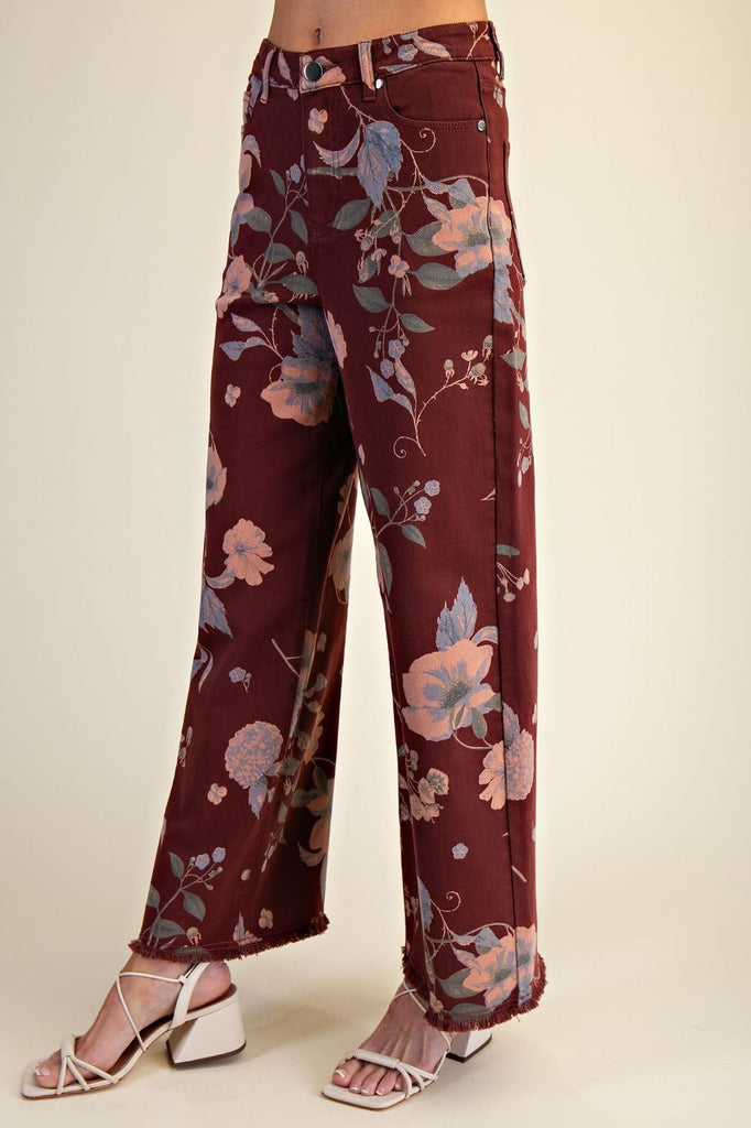 Model wearing Easel Calluna floral twill pants in burgundy with soft pink and blue botanical print, featuring high waist and straight leg silhouette.