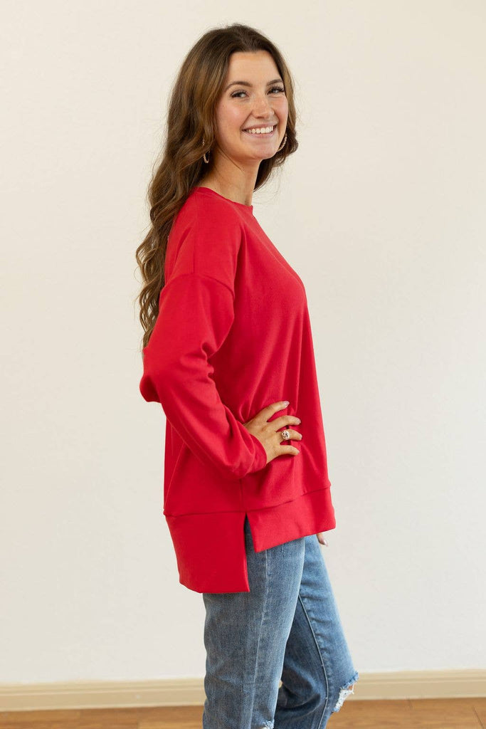 Model wearing the Carys Red Split Hem Pullover — a relaxed-fit red crewneck sweatshirt with long sleeves and a modern split hem.
