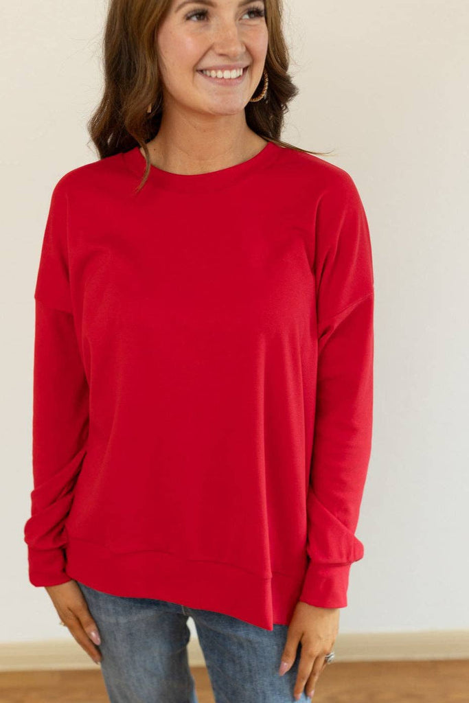 Model wearing the Carys Red Split Hem Pullover — a relaxed-fit red crewneck sweatshirt with long sleeves and a modern split hem.