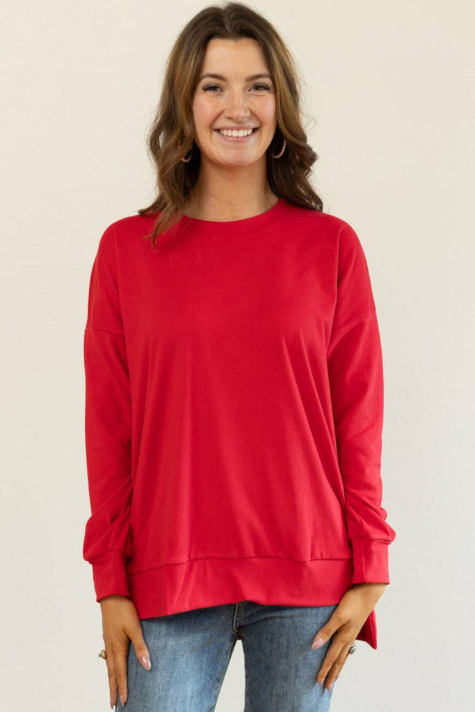Model wearing the Carys Red Split Hem Pullover — a relaxed-fit red crewneck sweatshirt with long sleeves and a modern split hem.