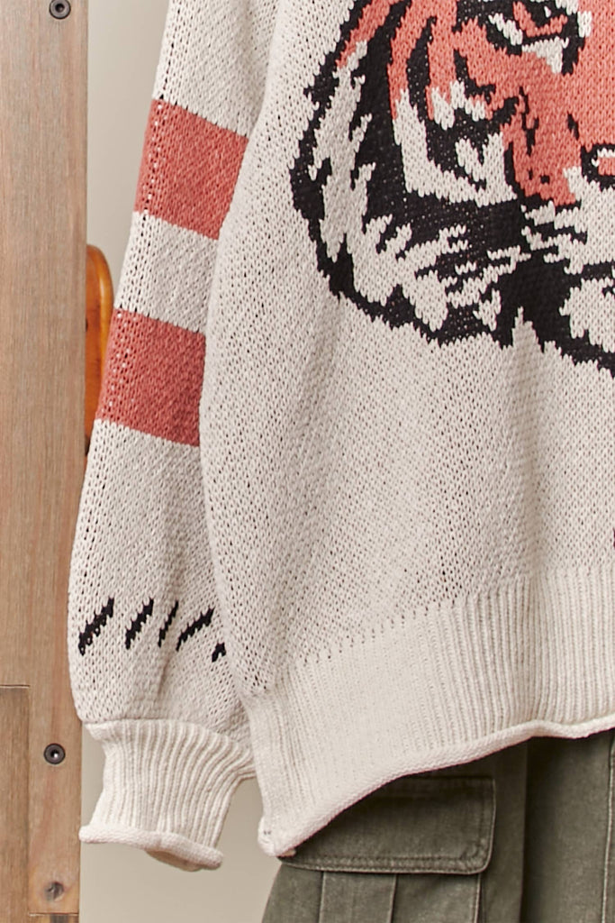 Cream knit sweater with a large tiger face graphic and rust stripe sleeves.