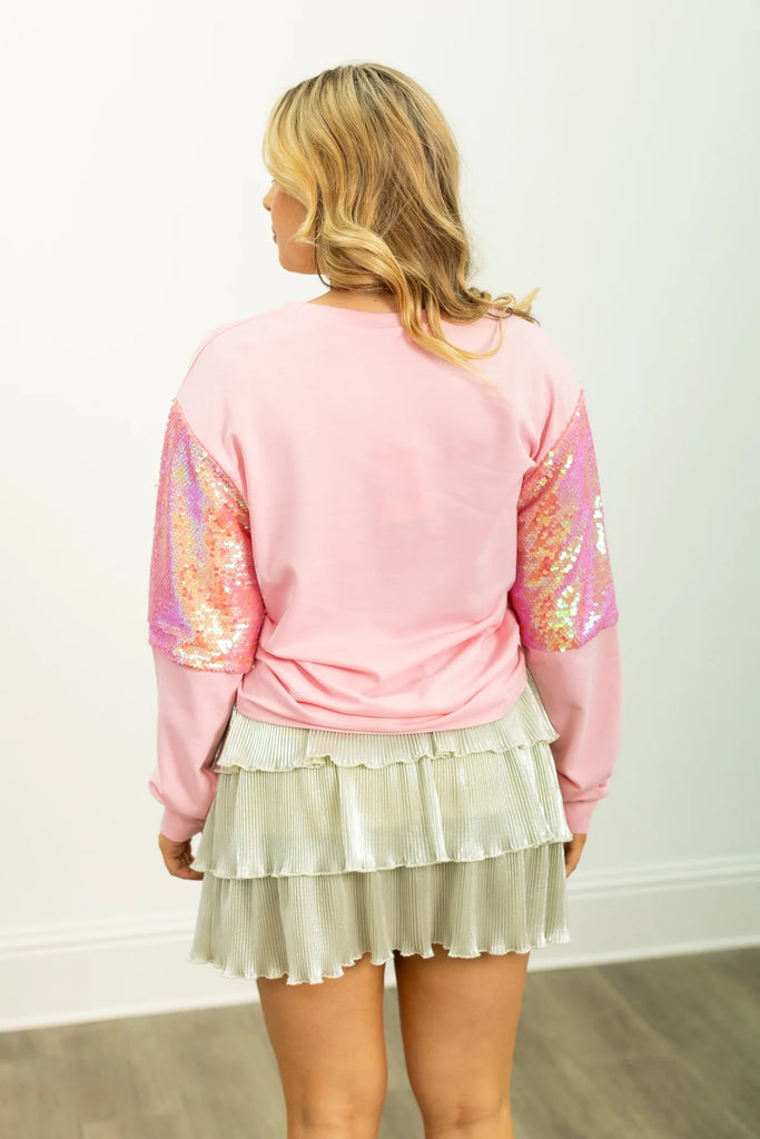 Chrissy Feelin' Festive sweatshirt in light pink with a gingerbread house graphic and iridescent sequin sleeves for a cheerful, holiday-ready style.