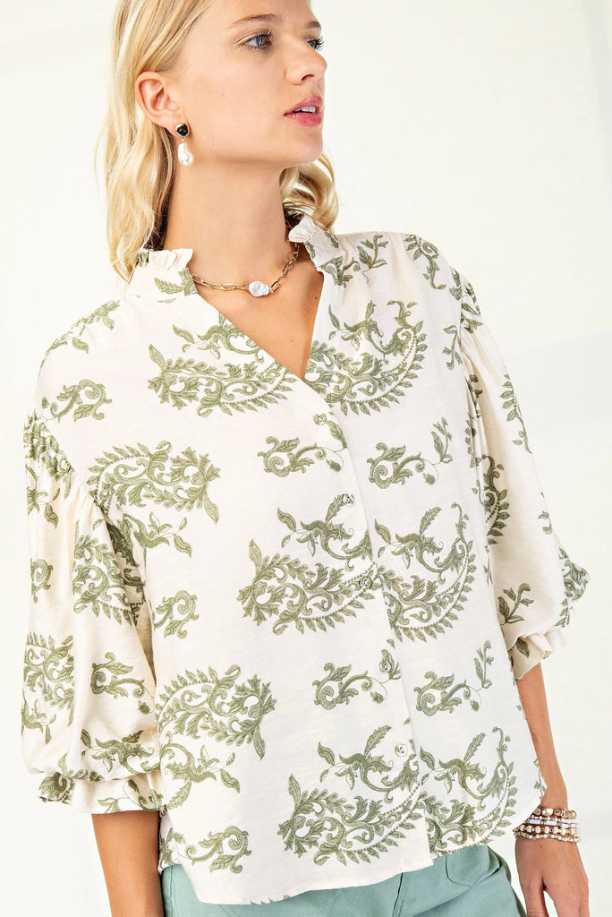 Woman wearing a cream button-down blouse with green embroidered floral patterns and 3/4 length balloon sleeves.