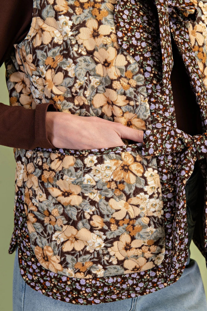 A quilted vest with a brown and cream floral print and two oversized bow ties on the front.