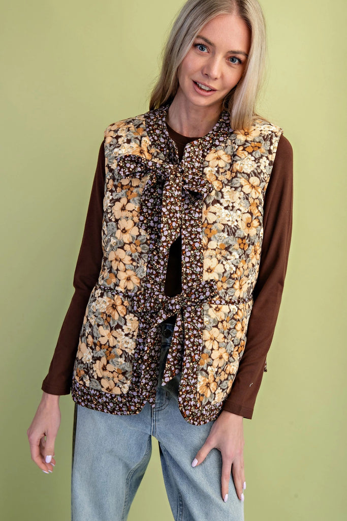 A quilted vest with a brown and cream floral print and two oversized bow ties on the front.