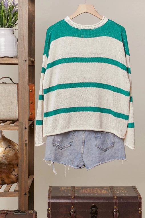 A green-and-cream striped knit sweater adorned with three-dimensional daisy flower appliques is displayed on a hanger, styled over distressed light blue denim shorts.