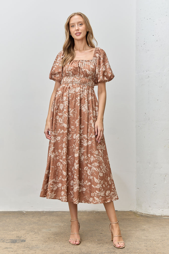Model wearing Isola Floral Textured Midi Dress in terracotta with cream floral print, puff sleeves, and smocked waist.