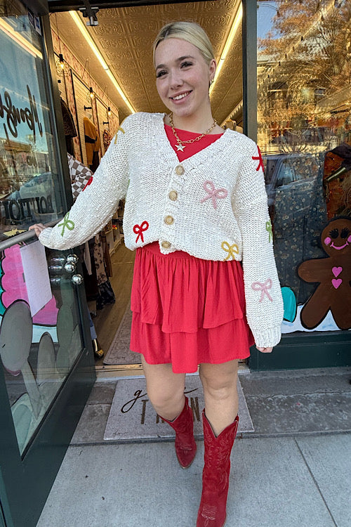Woman in a white cardigan with decorative buttons and red skirt standing in front of a store entrance.