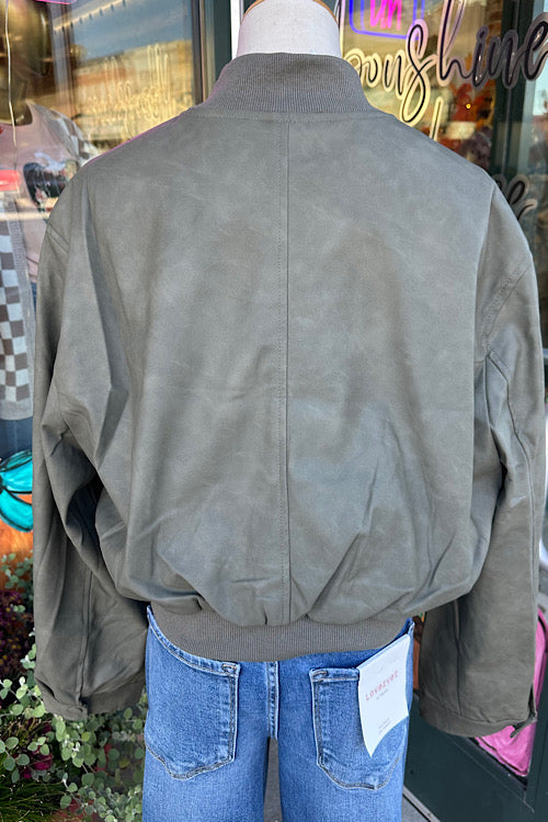 Person wearing a green jacket with a visible brand tag, standing in front of a store window.