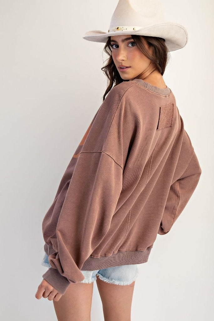 A mocha-colored, oversized pullover made of washed terry fabric. It has a large orange and tan bow graphic on the front, a crew neckline, and long sleeves.
