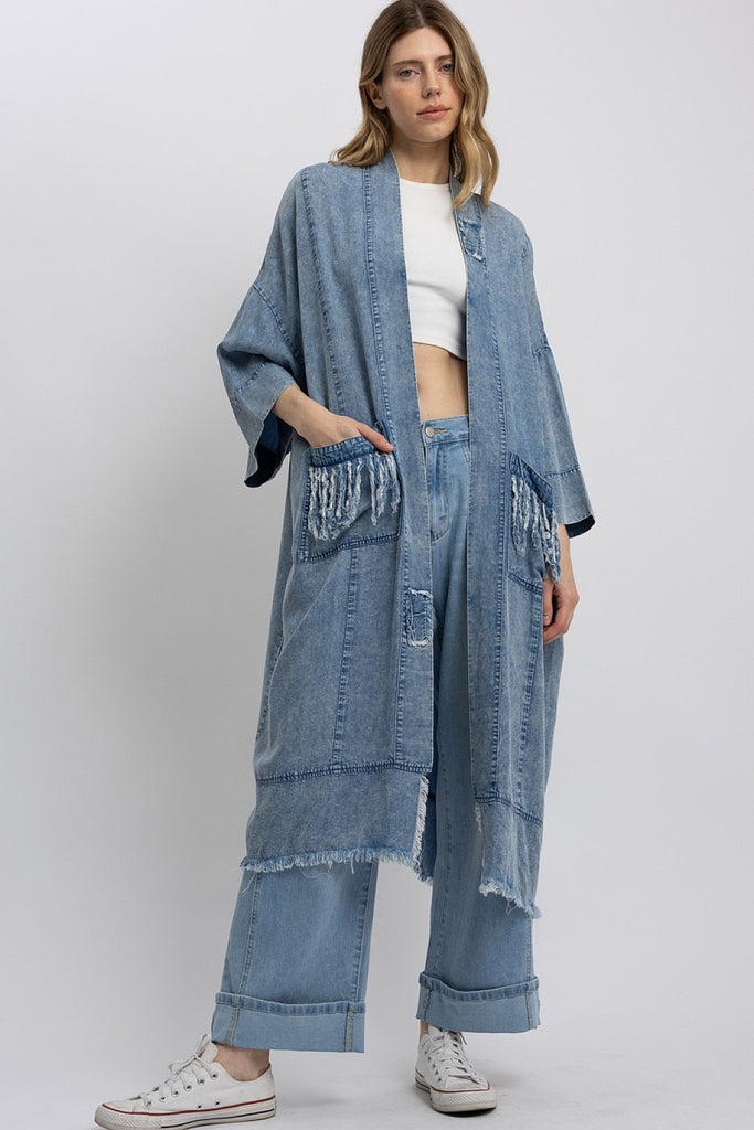 Front view of a model wearing a mid-length oversized denim kimono with a large paisley star patch and peace sign embroidery; front view shows fringe pocket details and relaxed open front styling.