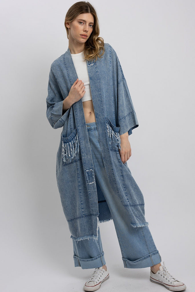 Back view of a model wearing a mid-length oversized denim kimono with a large paisley star patch and peace sign embroidery; front view shows fringe pocket details and relaxed open front styling.