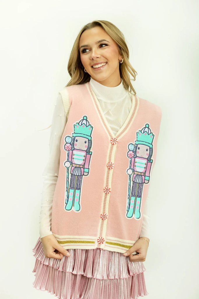 Southern Grace Giselle nutcracker sweater vest in pastel pink, with two embroidered nutcracker designs, candy cane buttons, and a ribbed V-neck trim."