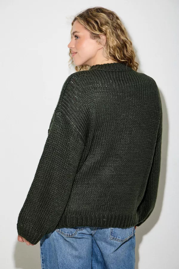 Model wearing Hadley Western Boot Sweater by Polagram in deep forest green featuring embroidered boots with red bow detail.