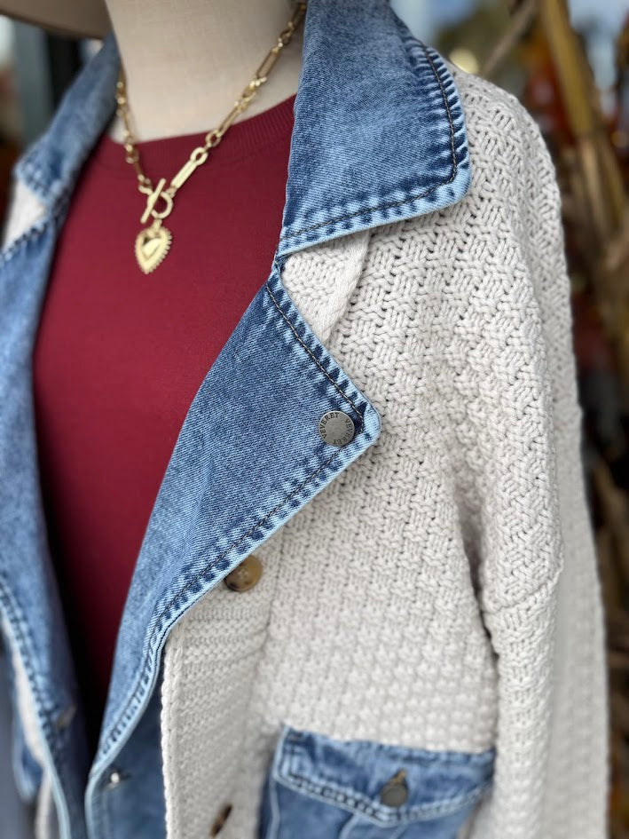 Mannequin wearing a denim jacket over a beige knitted cardigan with a blurred background