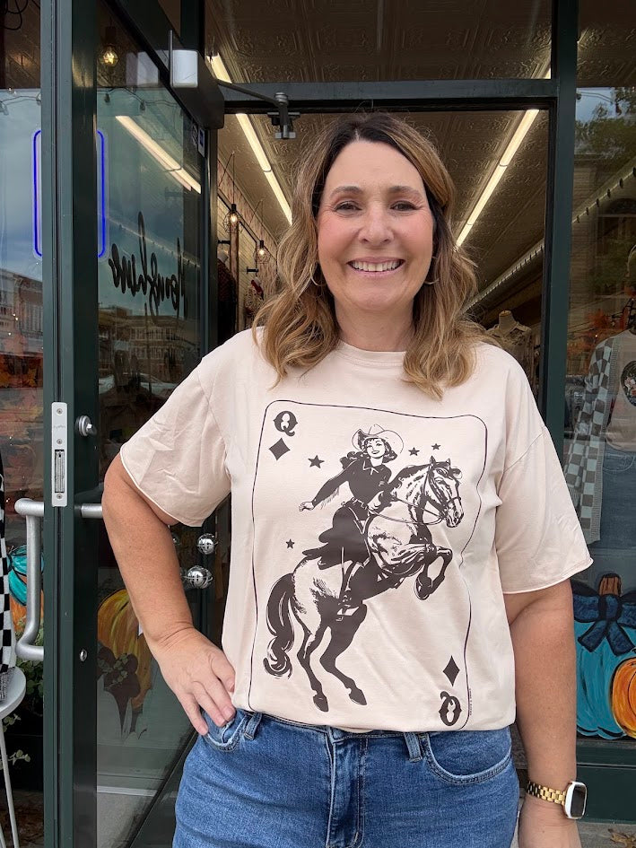 Woman wearing a t-shirt with a graphic design of a person on a horse, standing in front of a store entrance.
