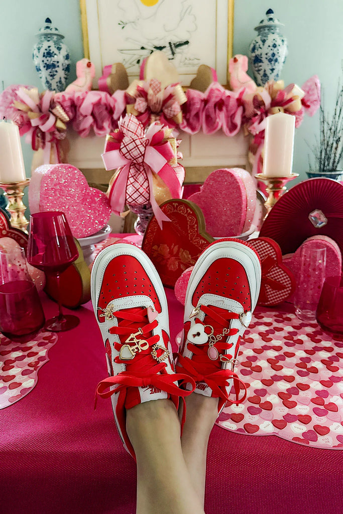 Red sneakers with white laces and decorative elements on a festive background with pink and red decorations.