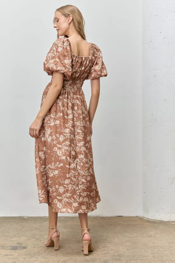 Model wearing Isola Floral Textured Midi Dress in terracotta with cream floral print, puff sleeves, and smocked waist.